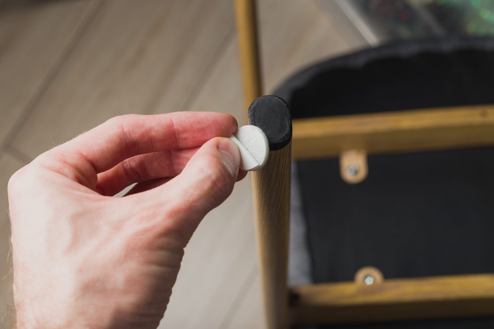 Hand klebt selbstklebendes Filzpad unter Stuhlbein auf Holzboden