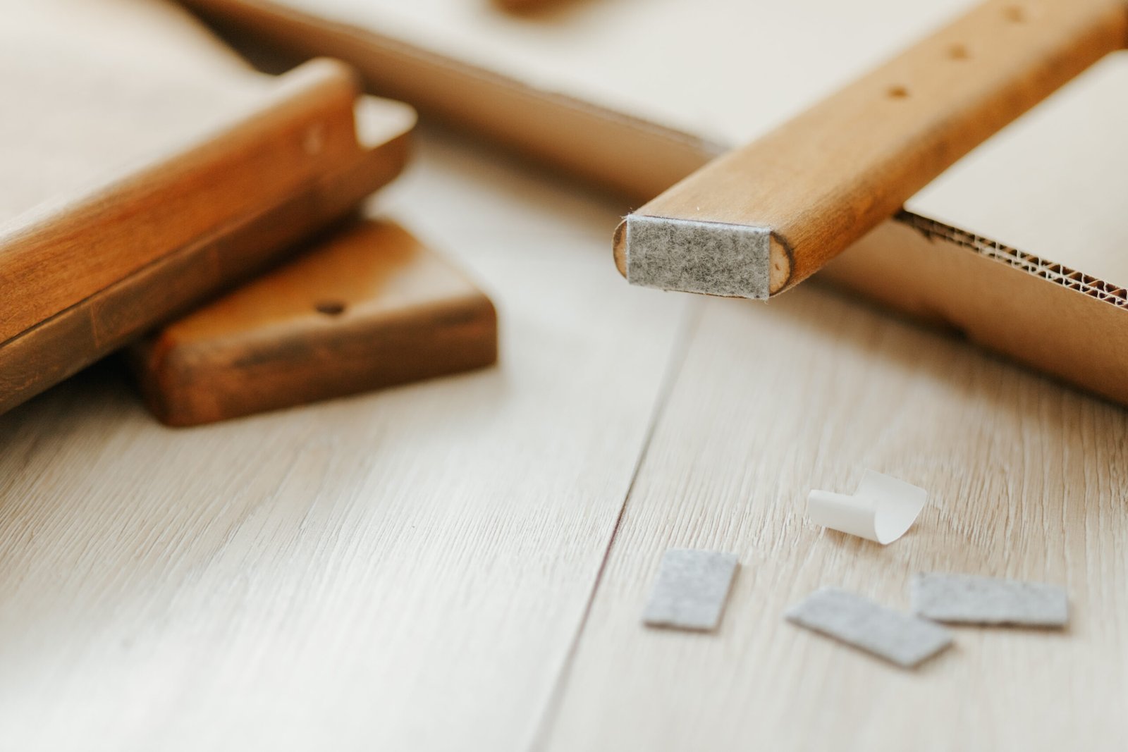 Möbelbeine mit Gleitern auf hellem Holzboden, daneben lose Möbelpads